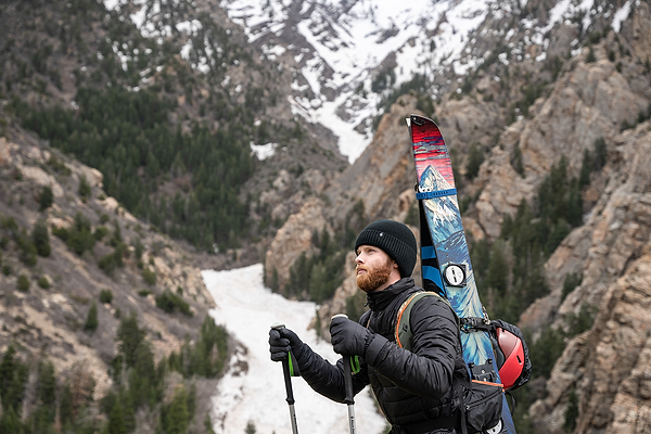 Man hikes up hill with skiing gear.