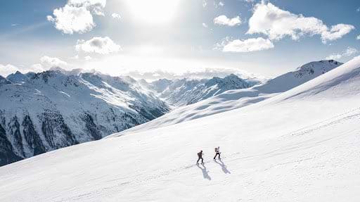 Two people hike up a remote, snow-filled hill.