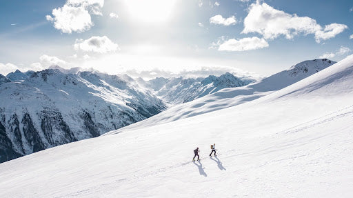 Two people hike up a remote, snow-filled hill.