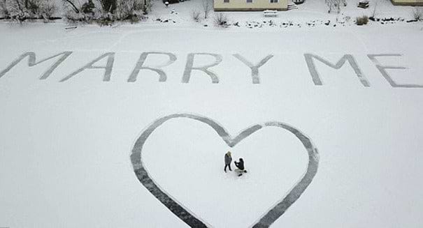 Aerial view of a proposal message written in snow covered ice with a man proposing to a woman.