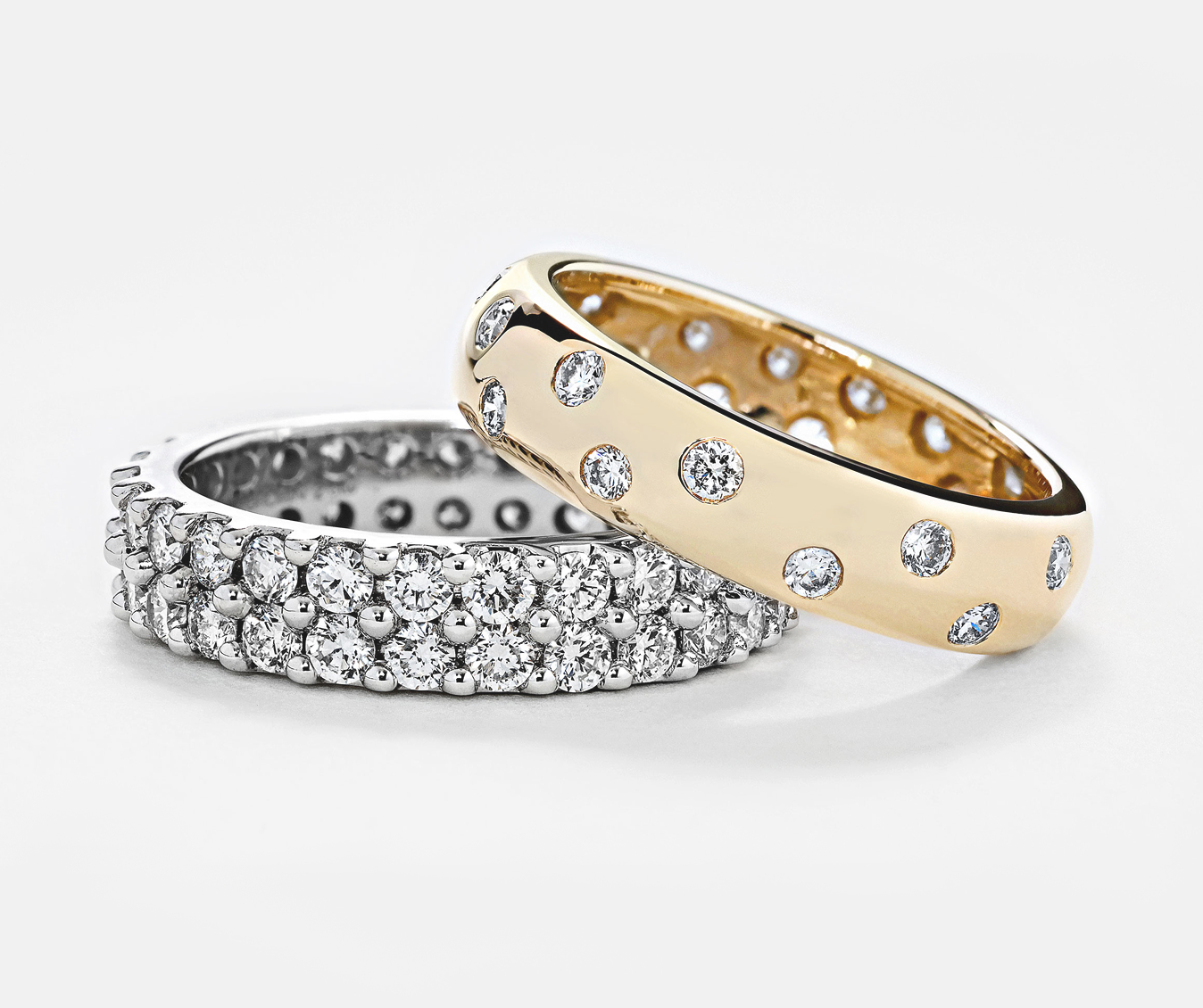 A wedding band and eternity band, one gold and one silver, on a light gray background.