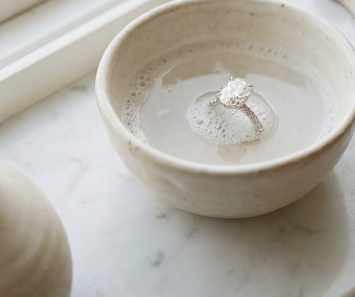 lab-grown diamond engagement ring sitting in a white ceramic bowl on a marble surface
