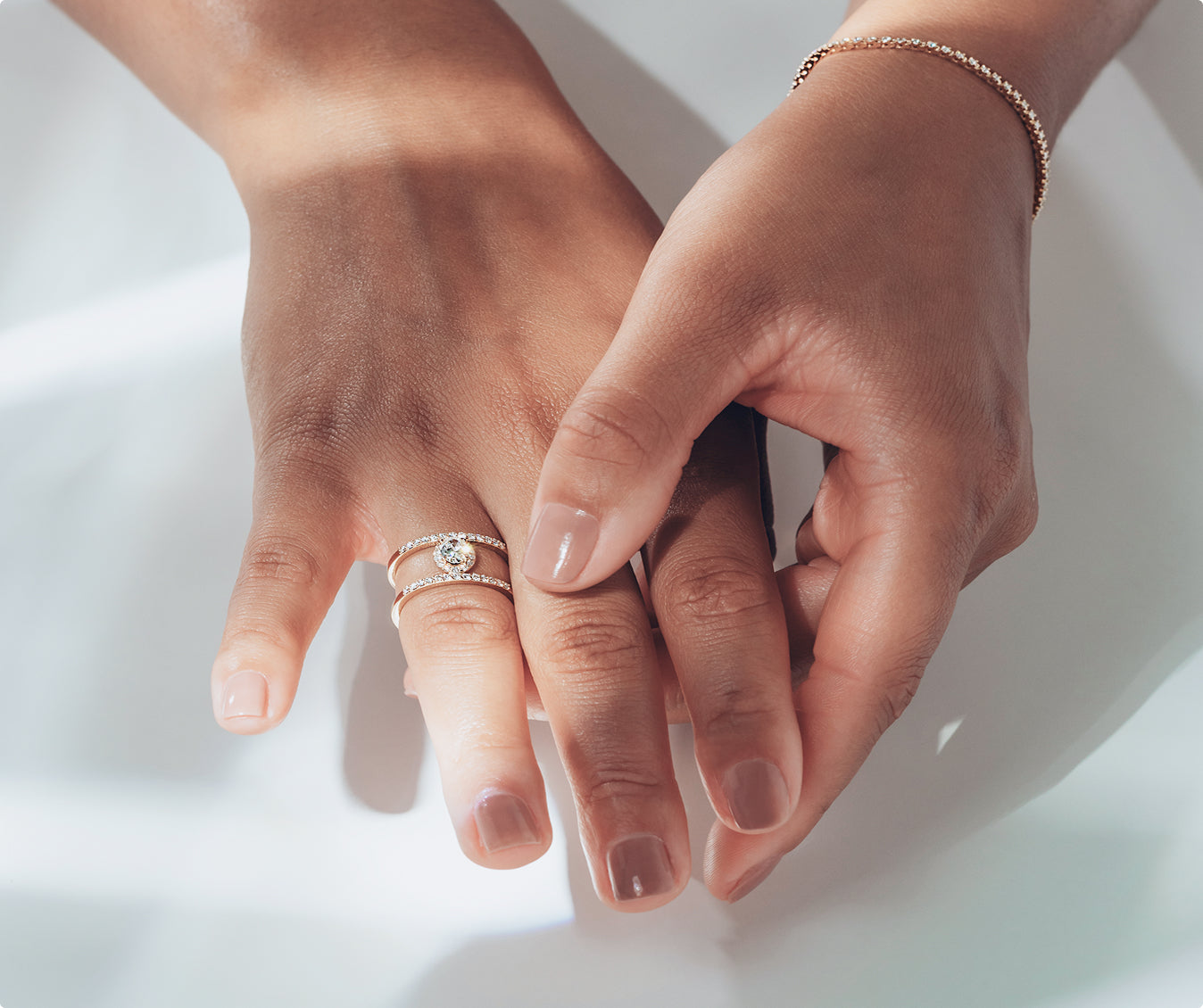 Close-up of two hands with a round cut engagement ring on a light background