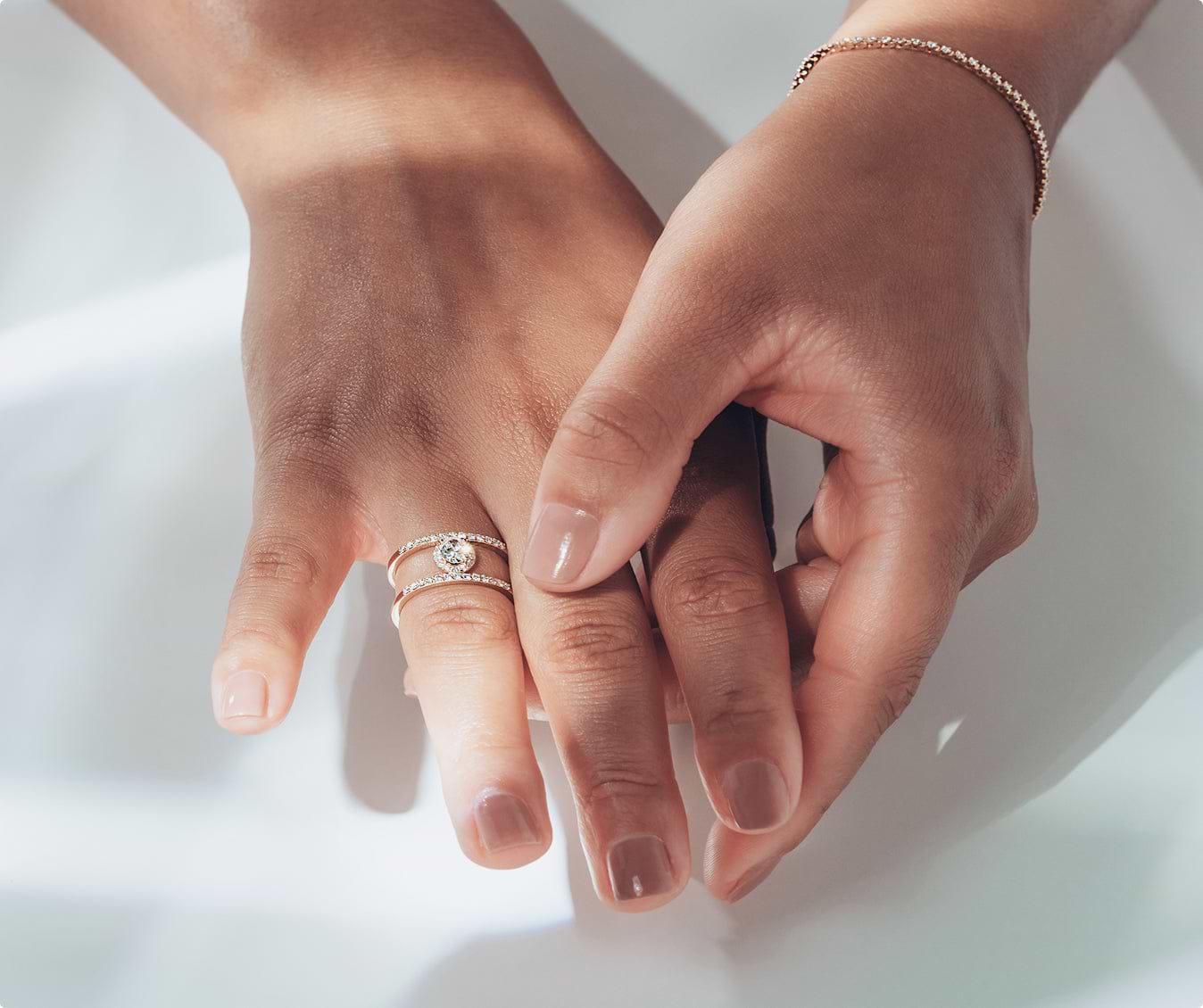Close-up of two hands with a round cut engagement ring on a light background
