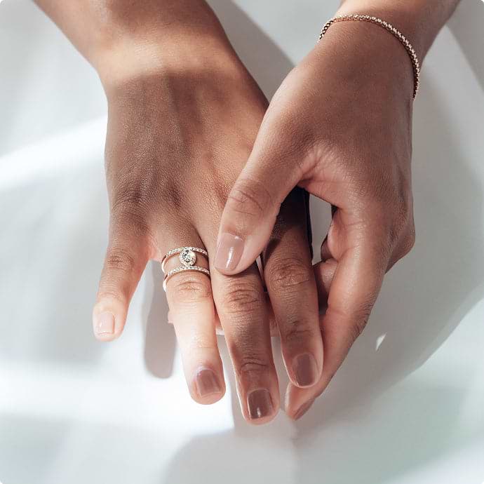 Close-up of two hands with a round cut engagement ring on a light background