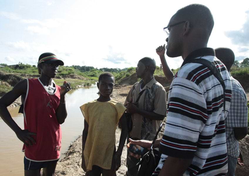A group of people congregate near a stream at THE GREENER DIAMOND FARM in SIERRA LEONE