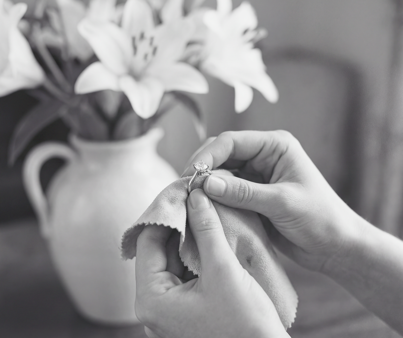Person cleaning a diamond ring with a cloth, with flowers in the background