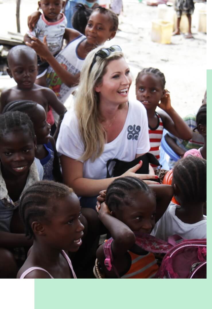 Smiling MiaDonna CEO Anna-Mieke Anderson surrounded by a cheerful group of children at a The Greener Diamond location in Liberia.