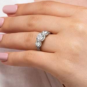 Luxurious three stone engagement ring with round cut lab grown diamonds surrounded by diamond halos in 14k white gold worn on hand