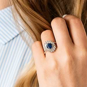Unique stunning vintage style diamond halo engagement ring with baguette cut diamonds surrounding a 1ct round cut lab grown blue sapphire in 14k white gold worn on hand