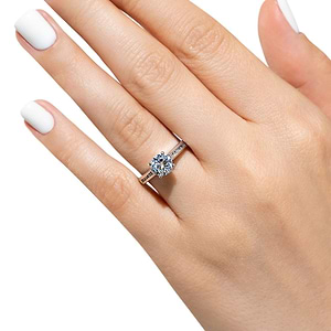 Modern diamond accented engagement ring with 1ct round cut lab grown diamond and channel set princess cut accenting side stones in 14k rose gold worn on hand