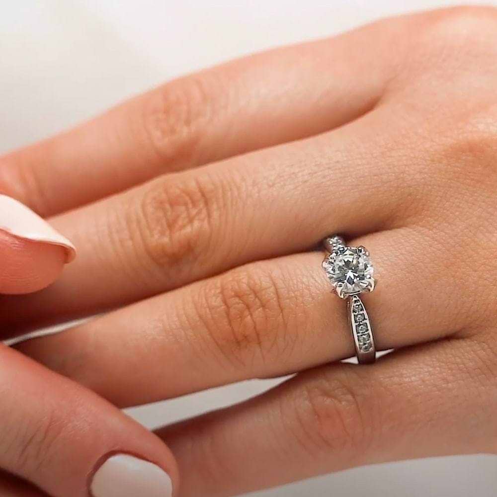Shown with 1ct Round Cut Lab Grown Diamond in 14k White Gold|Beautiful channel set diamond accented engagement ring with 1ct round cut lab grown diamond and peek-a-boo diamonds in 14k white gold band