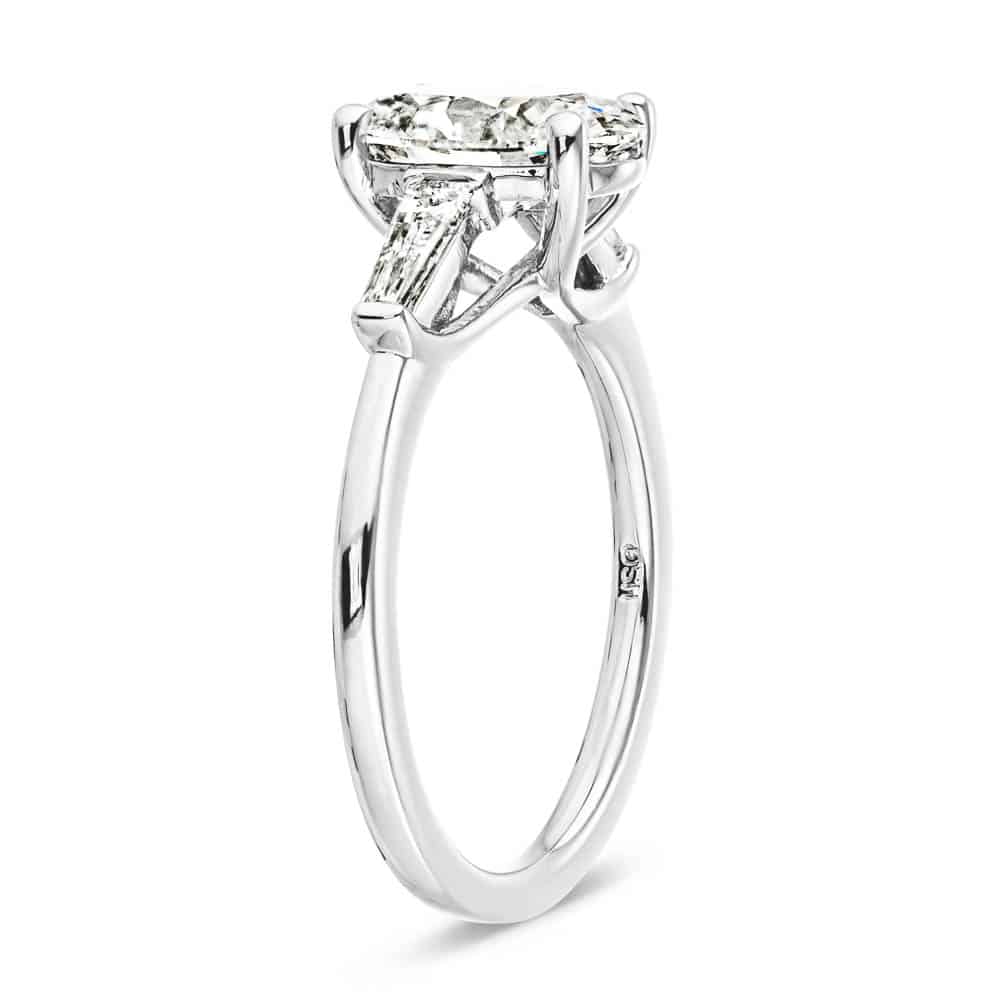 Shown with 2ct Oval Cut Lab Grown Diamond set in 14k White Gold|Beautiful three stone engagement ring with trellis set 2ct oval cut lab grown diamond amid baguette side stones in 14k white gold shown from side