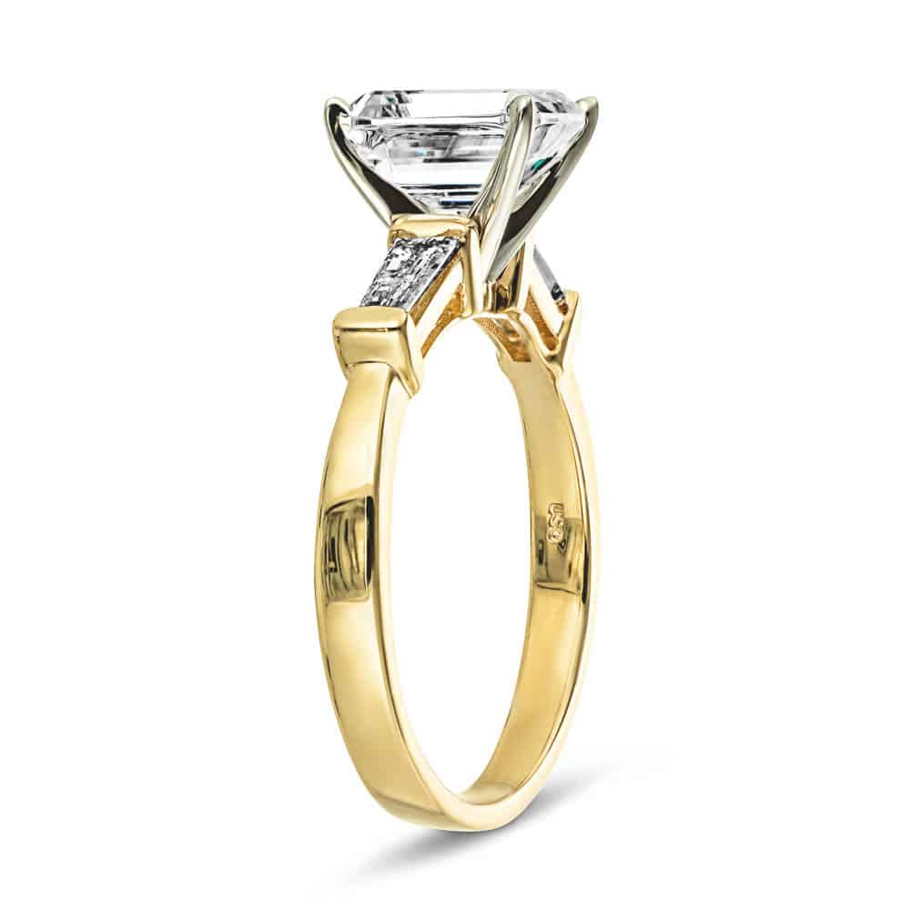 Shown with 1.5ct Emerald Cut Lab Grown Diamond in 14k Yellow Gold|Modern three stone engagement ring with two baguette cut recycled diamond side stones and a 1.5ct emerald cut lab grown diamond center in 14k yellow gold shown from side