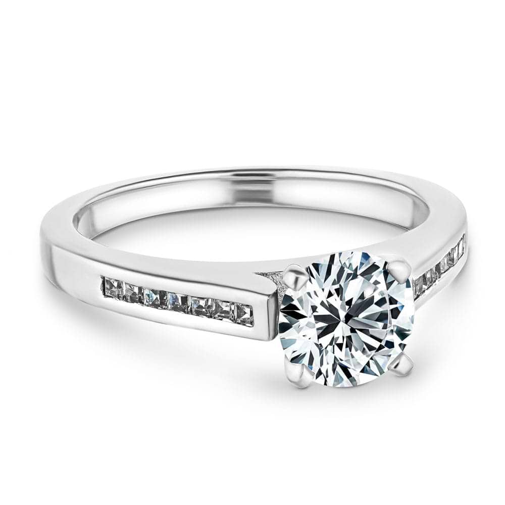 Shown with 1ct Round Cut Lab Grown Diamond in Platinum|Modern style diamond accented engagement ring with 1ct round cut lab grown diamond and channel set princess cut accenting side stones in platinum