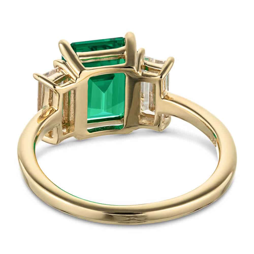 Shown with 2ct Emerald Cut Lab Grown Emerald with 2 Baguette Cut Lab Diamonds in 14k Yellow Gold|Three stone basket set engagement ring with green emerald and yellow gold shown from back