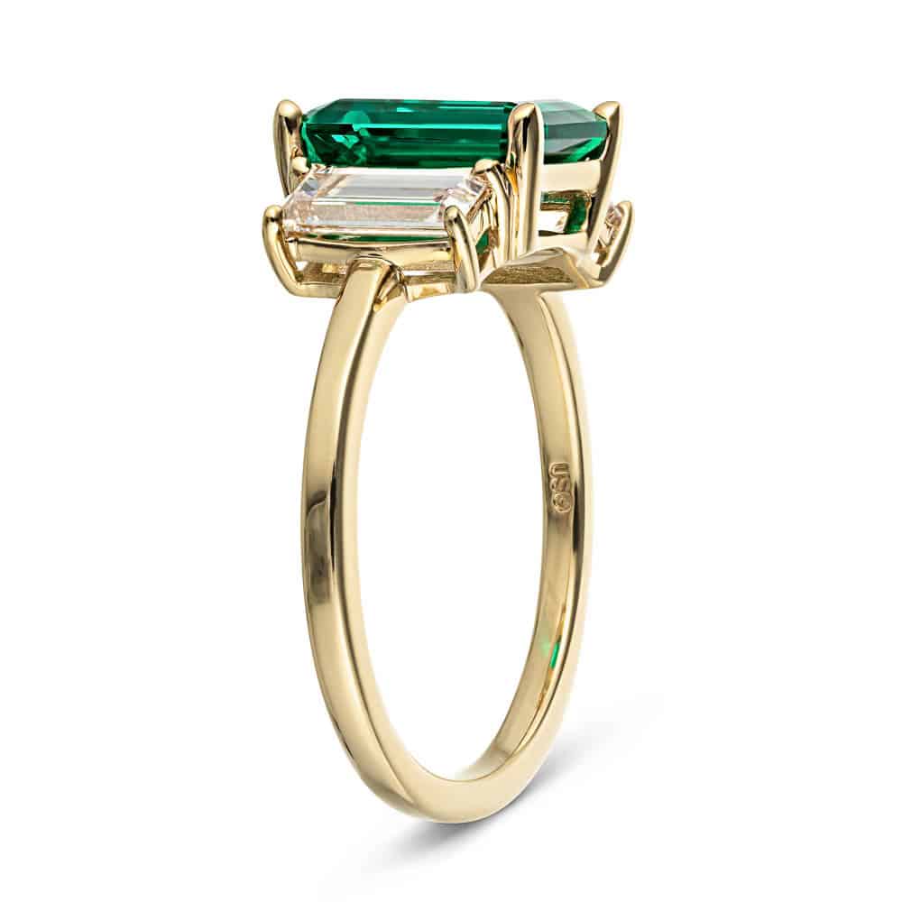 Shown with 2ct Emerald Cut Lab Grown Emerald with 2 Baguette Cut Lab Diamonds in 14k Yellow Gold|Three stone basket set engagement ring with green emerald and yellow gold shown from side