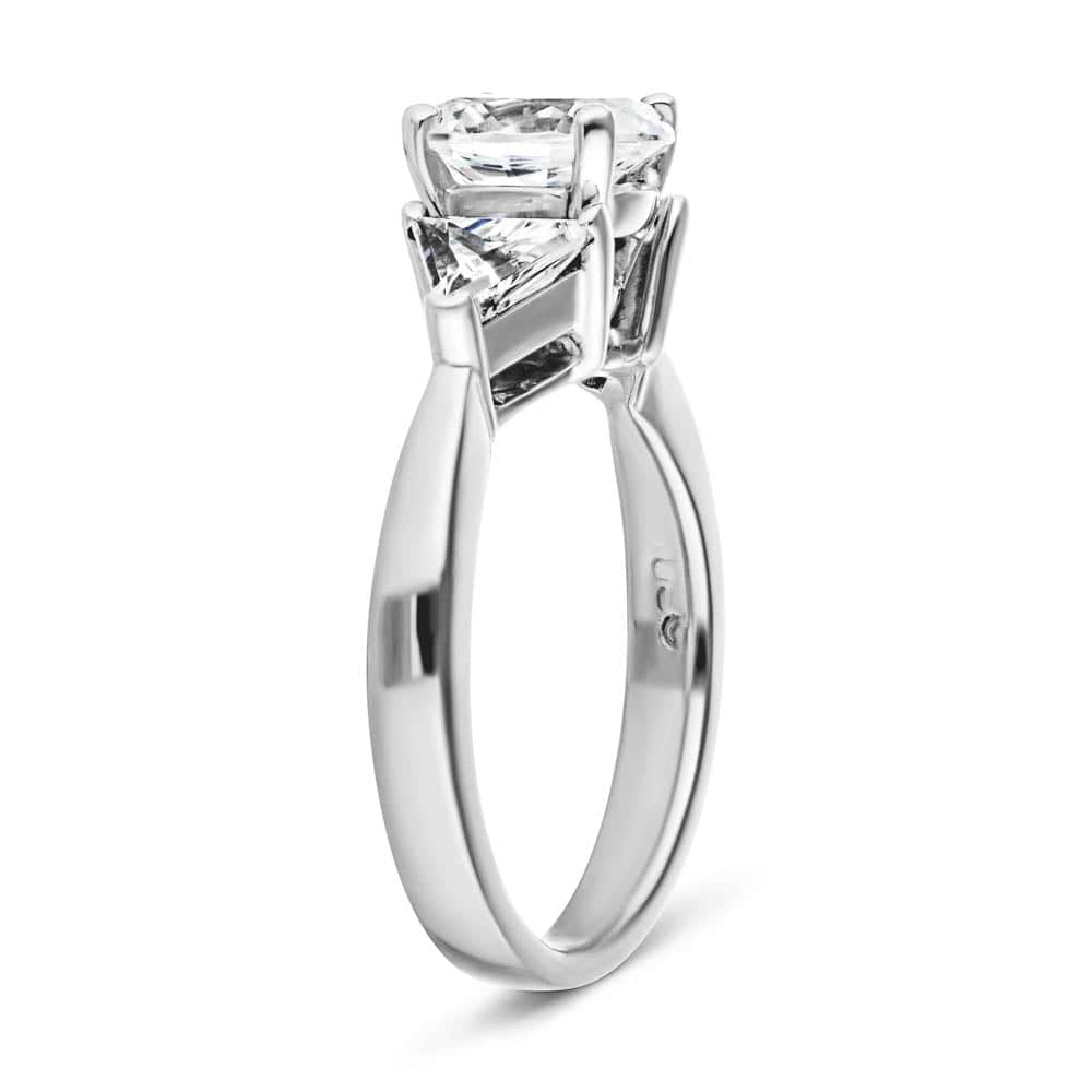 Shown with 1ct Oval Cut Lab Grown Diamond & 0.50ct Triangle Cut Side Stones in 14k White Gold|Three stone engagement ring with 1ct oval cut lab grown diamond and two 0.50 triangle cut diamond side stones in 14k white gold band shown from side