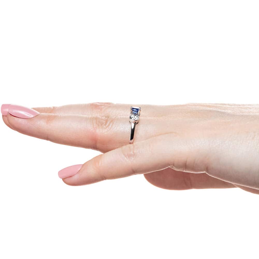 Shown with Round Cut Lab Grown Diamonds on either side of a Lab Created Blue Sapphire in 14k White Gold|Three stone engagement with round cut lab grown diamonds and lab created blue sapphire center stone in 14k white gold worn on hand