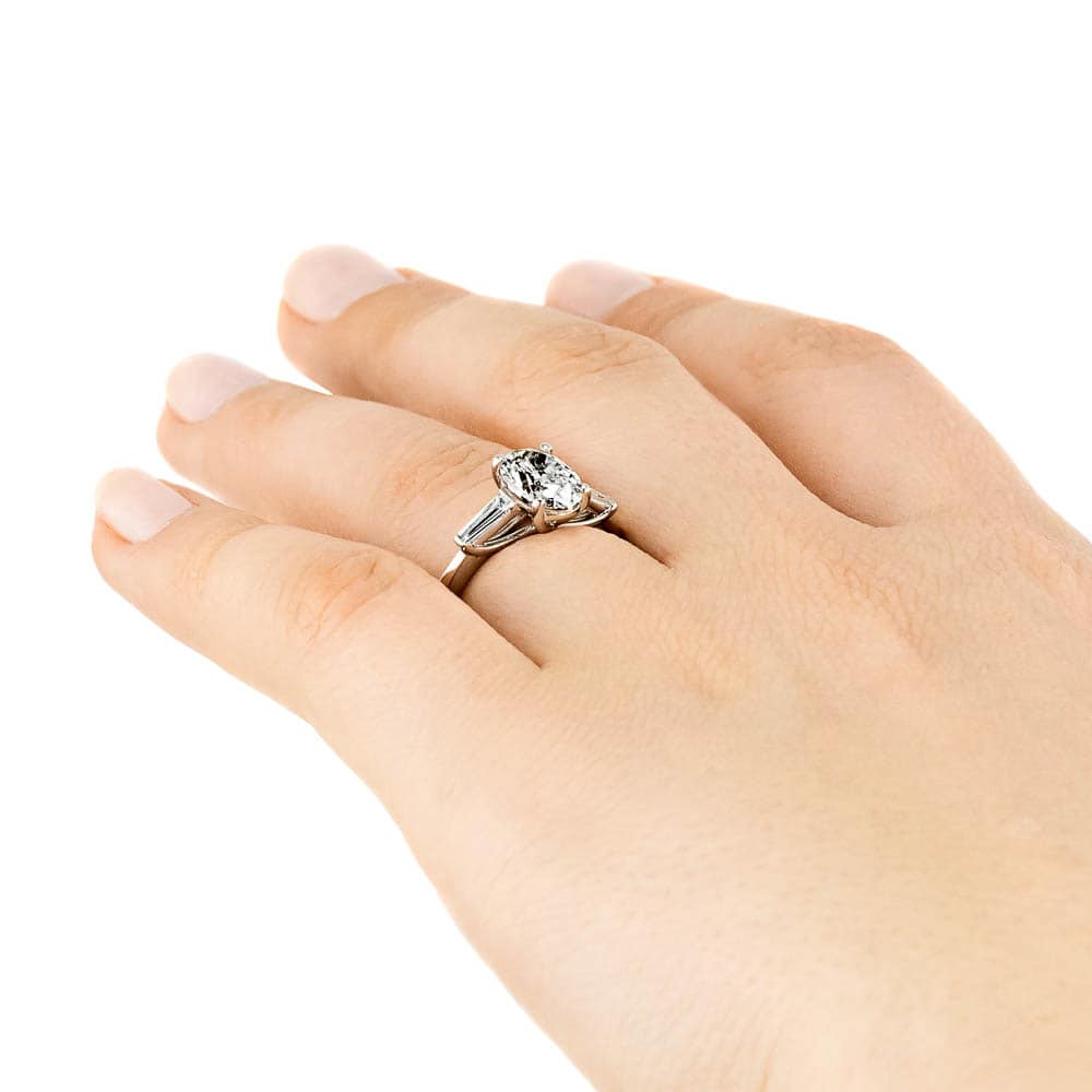 Shown with 2ct Oval Cut Lab Grown Diamond set in 14k White Gold|Beautiful three stone engagement ring with trellis set 2ct oval cut lab grown diamond amid baguette side stones in 14k white gold shown worn on hand