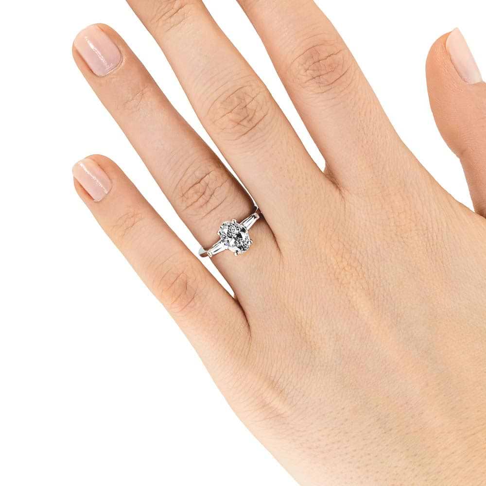 Shown with 2ct Oval Cut Lab Grown Diamond set in 14k White Gold|Beautiful three stone engagement ring with trellis set 2ct oval cut lab grown diamond amid baguette side stones in 14k white gold shown worn on hand