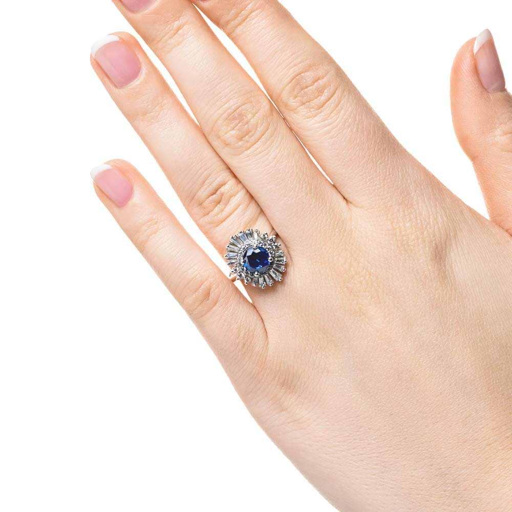 Shown with 1ct Round Cut Lab Grown Blue Sapphire|Unique stunning vintage style diamond halo engagement ring with baguette cut diamonds surrounding a 1ct round cut lab grown blue sapphire in 14k white gold worn on hand