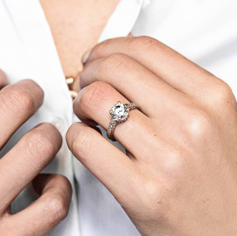 Shown with 1ct Round Cut Lab Grown Diamond in 14k White Gold|Vintage style diamond accented engagement ring with 1ct round cut lab grown diamond in 14k white gold filigree detailed band shown worn on hand