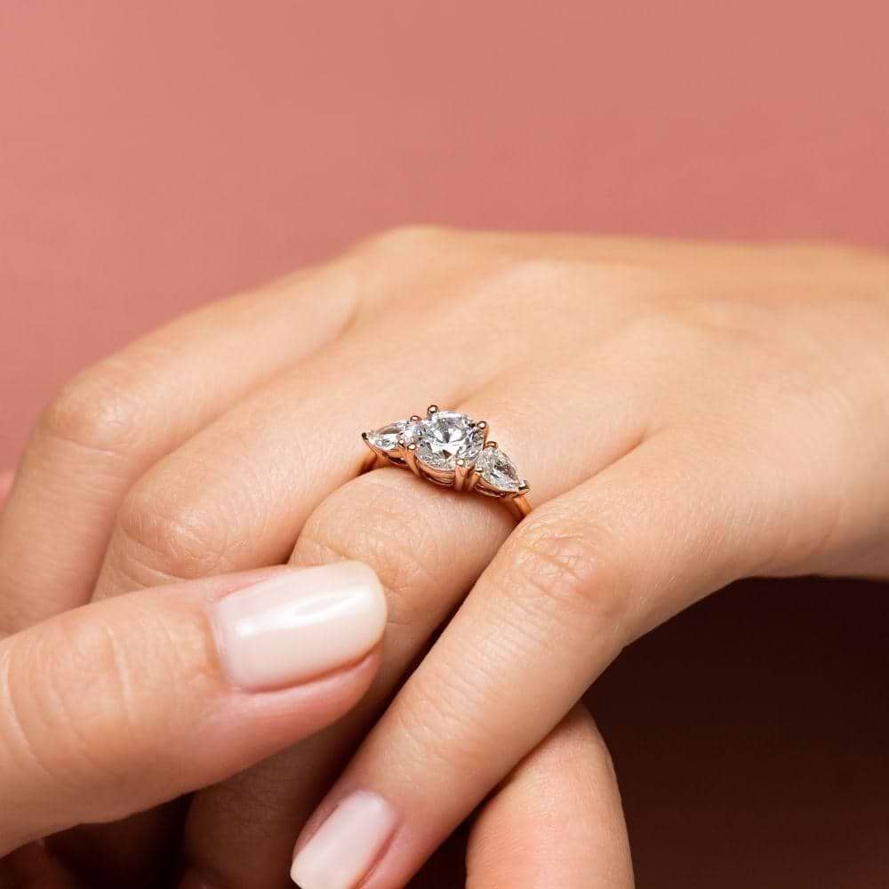 Shown with 1ct Round Cut Lab Grown Diamond Center Stone in 14k White Gold|Conflict-free three stone engagement ring with 1ct round cut lab grown diamond center and 0.5ct pear cut diamond side stones in 14k white gold worn on hand