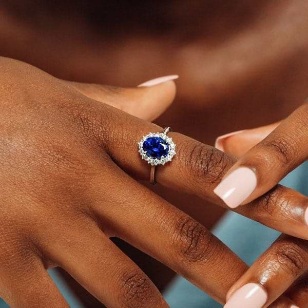 Shown with 3ct Oval Cut Lab Grown Blue Sapphire in 14k White Gold|Ethical vintage style engagement ring with floral design halo around a 3ct lab created blue sapphire in 14k white gold worn on hand
