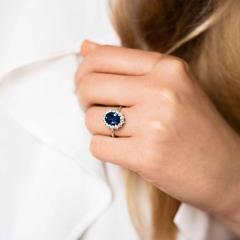 Shown with 3ct Oval Cut Lab Grown Blue Sapphire in 14k White Gold|Beautiful vintage style engagement ring with floral design halo around a 3ct lab created blue sapphire in 14k white gold worn on hand