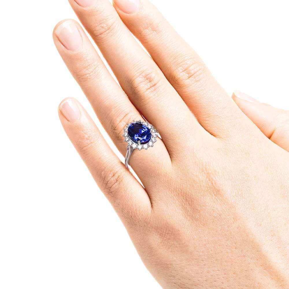 Shown with 3ct Oval Cut Lab Grown Blue Sapphire in 14k White Gold|Vintage style engagement ring with floral design halo around a 3ct lab created blue sapphire in 14k white gold worn on hand