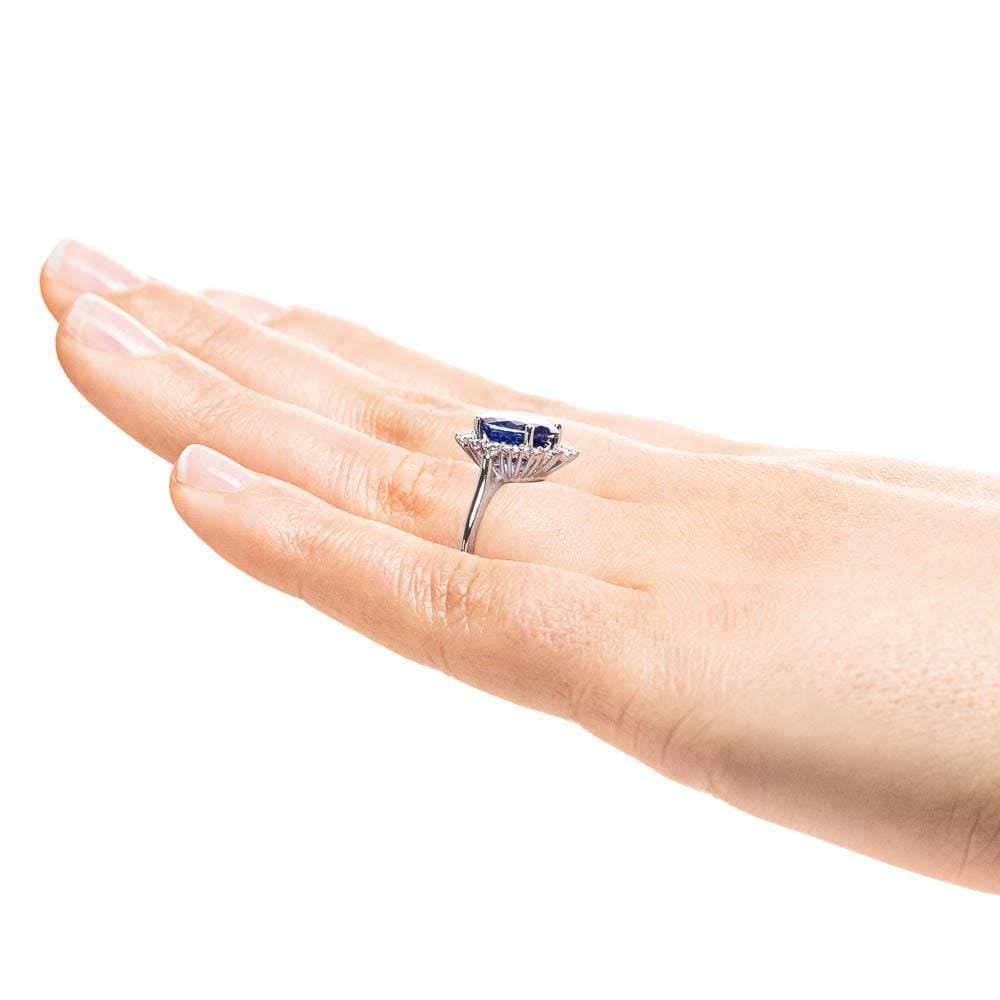 Shown with 3ct Oval Cut Lab Grown Blue Sapphire in 14k White Gold|Vintage style engagement ring with floral design halo around a 3ct lab created blue sapphire in 14k white gold worn on hand sideview