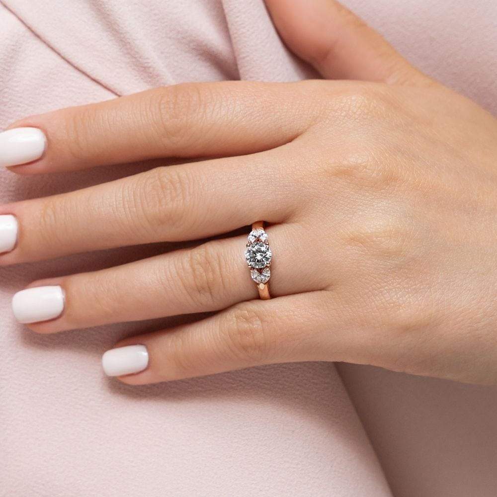 Shown with 0.75ct Round Cut Lab Grown Diamond Center in 14k Rose Gold|Unique romantic diamond accented engagement ring with 0.75ct round cut lab grown diamond center and 4 marquise cut side stones in 14k rose gold shown worn on hand