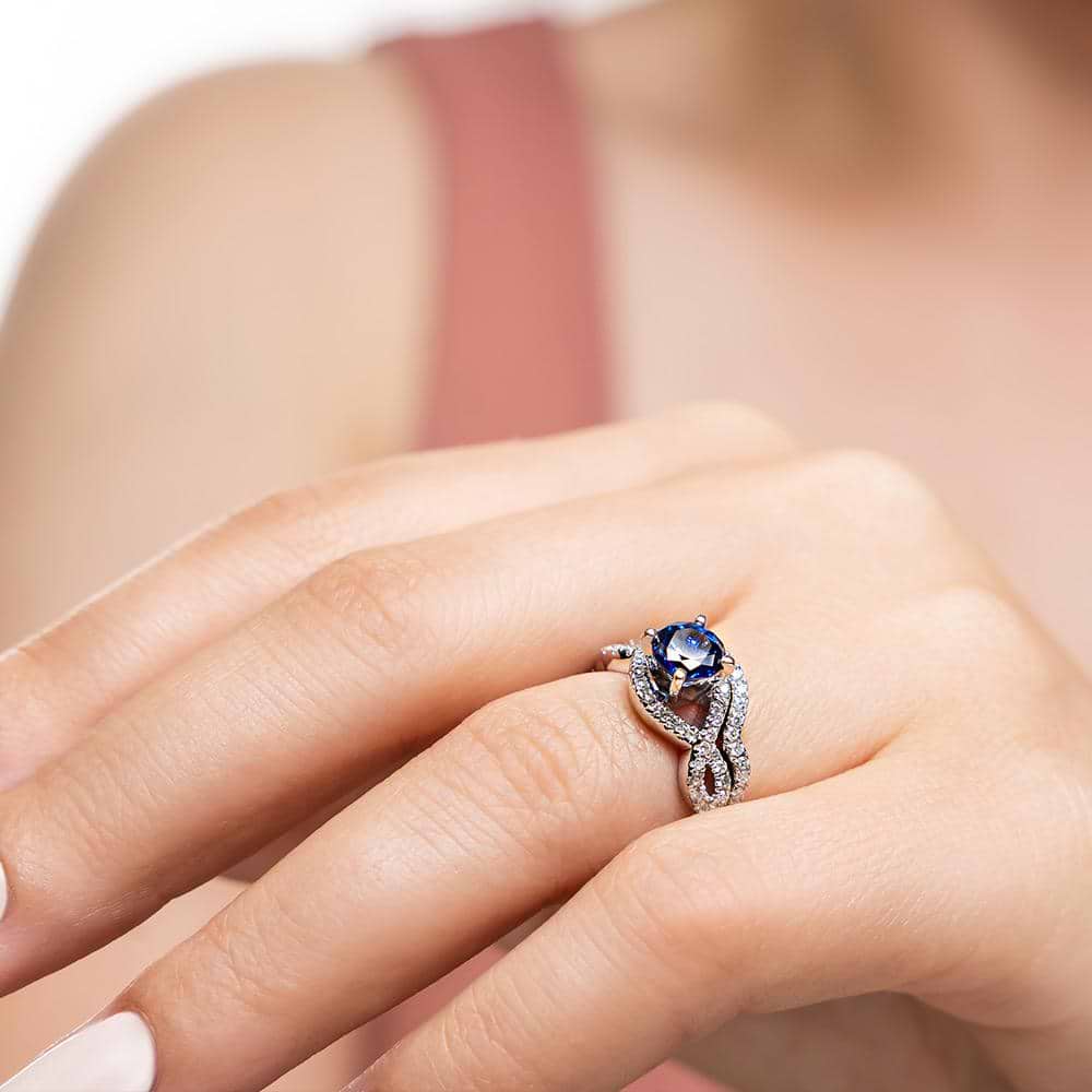 Shown with a 1.0ct Round cut Blue Sapphire Lab-Created Gemstone with infinity style diamond accented band with matching wedding band | wedding set Shown with a 1.0ct Round cut Blue Sapphire Lab-Created Gemstone with infinity style diamond accented band with matching wedding band