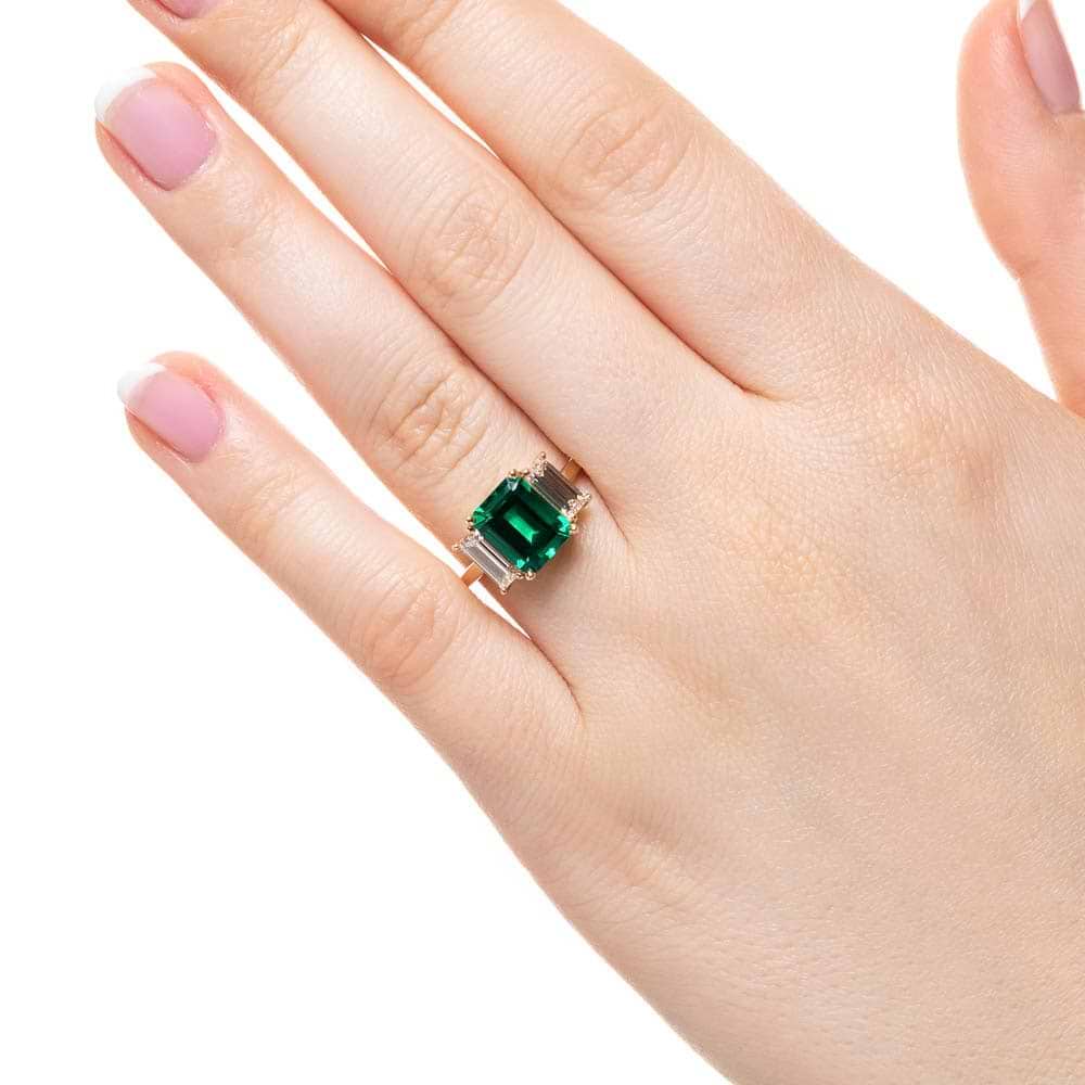 Shown with 2ct Emerald Cut Lab Grown Emerald with 2 Baguette Cut Lab Diamonds in 14k Yellow Gold|Three stone engagement ring with 2ct emerald cut lab created emerald center between baguette cut lab diamonds set in 14k yellow gold worn on hand