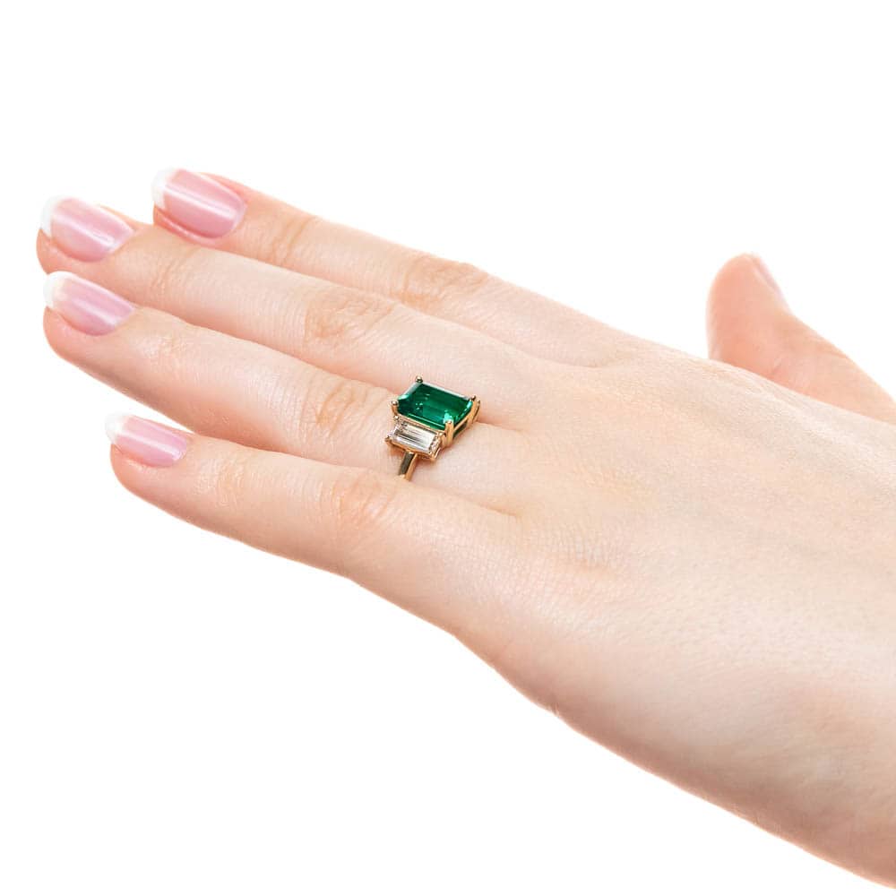 Shown with 2ct Emerald Cut Lab Grown Emerald with 2 Baguette Cut Lab Diamonds in 14k Yellow Gold|Three stone engagement ring with 2ct emerald cut lab created emerald center between baguette cut lab diamonds set in 14k yellow gold worn on hand sideview