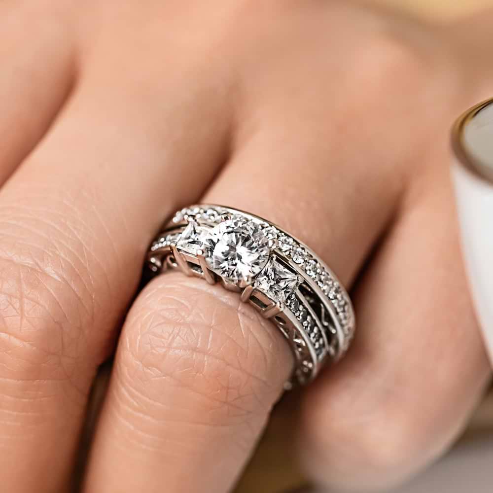 Shown with a Round cut center stone and two Princess cut Lab-Grown Diamonds side stones with scroll detailing and accenting diamonds on the band in recycled 14K white gold | three stone engagement ring Shown with round cut center stone and two Princess cut Lab-Grown Diamonds with scroll detailing and accenting diamonds on the band in recycled 14K white gold with matching wedding band
