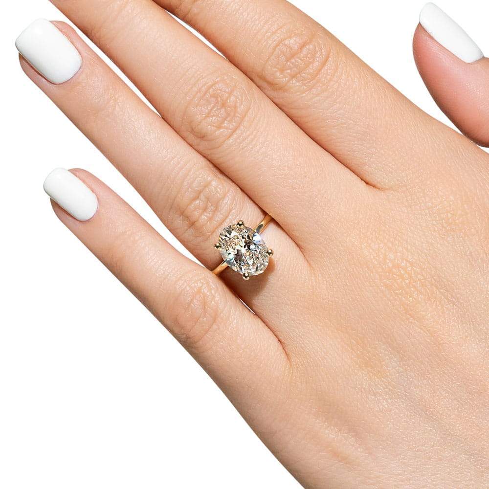 Shown with 3ct Oval Cut Lab Grown Diamond in 14k Yellow Gold|Elegant hidden halo engagement ring with 4 prong set 3ct oval cut lab grown diamond in a thin 14k yellow gold band worn on hand