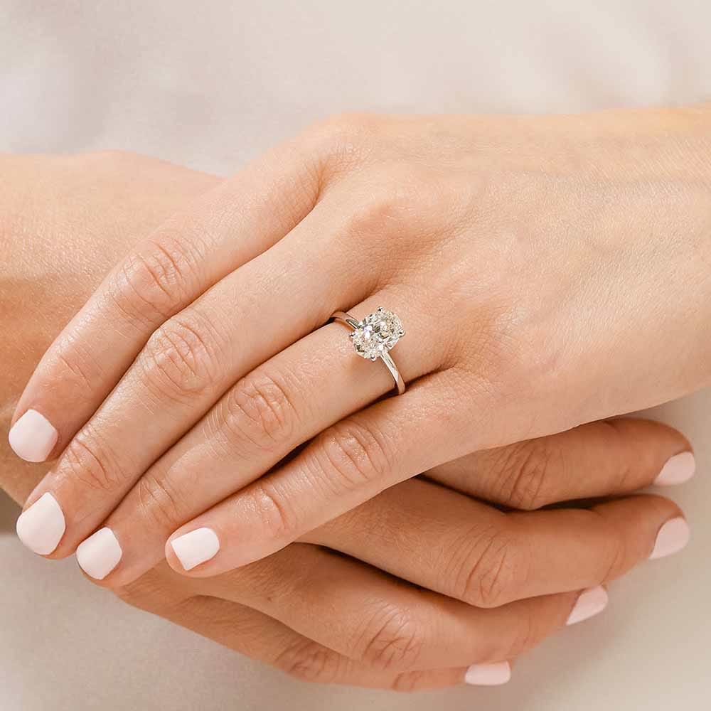 Shown with 2ct Oval Cut Lab Grown Diamond in 14k White Gold|Simple hidden halo engagement ring with 4 prong set 2ct oval cut lab grown diamond in a thin 14k white gold band worn on hand