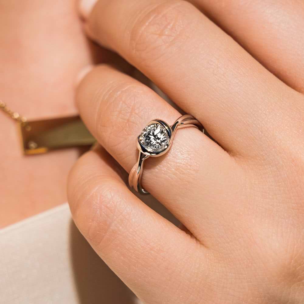Shown with 1ct Round Cut Lab Grown Diamond in Platinum|Unique modern ethical engagement ring with twisted band design holding a 1ct round cut lab grown diamond in platinum setting worn on hand