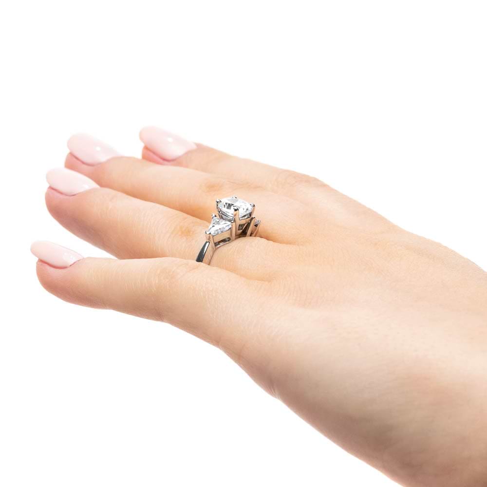 Shown with 1ct Oval Cut Lab Grown Diamond & 0.50ct Triangle Cut Side Stones in 14k White Gold|Three stone engagement ring with 1ct oval cut lab grown diamond and two 0.50 triangle cut diamond side stones in 14k white gold band worn on hand sideview