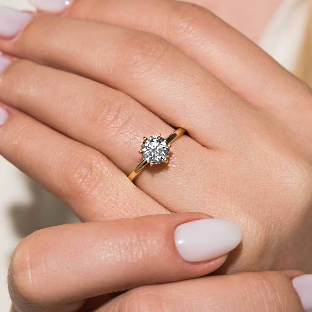 Traditional solitaire engagement ring shown here with a 1.5ct round lab-grown diamond in a six prong yellow gold setting. | Lab-grown diamond yellow gold six prong solitaire engagement ring