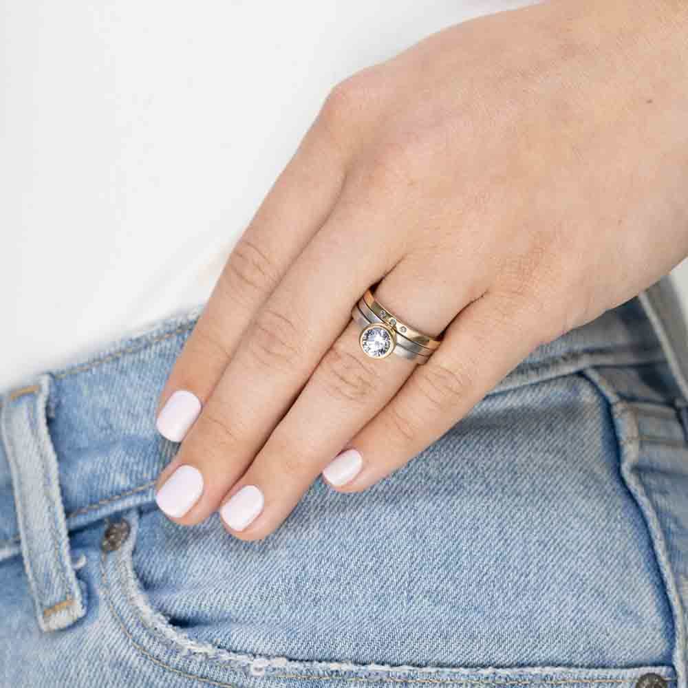 Shown in Two Toned 14K White Gold and 14K Yellow Gold Stacked with Mixed Metal Artisan Bands|bezel set solitaire engagement ring with round cut lab grown diamond in satin finish two tone white gold and yellow gold metal stacked with mixed metal stackable wedding bands