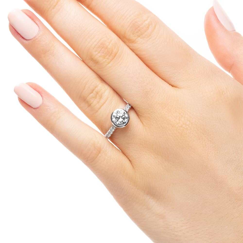 Shown with a bezel set 1.0ct Round cut Lab-Grown Diamond with accenting stones on the band in recycled 14K white gold | stackable engagement ring Shown with a bezel set 1.0ct Round cut Lab-Grown Diamond with accenting stones on the band in recycled 14K white gold