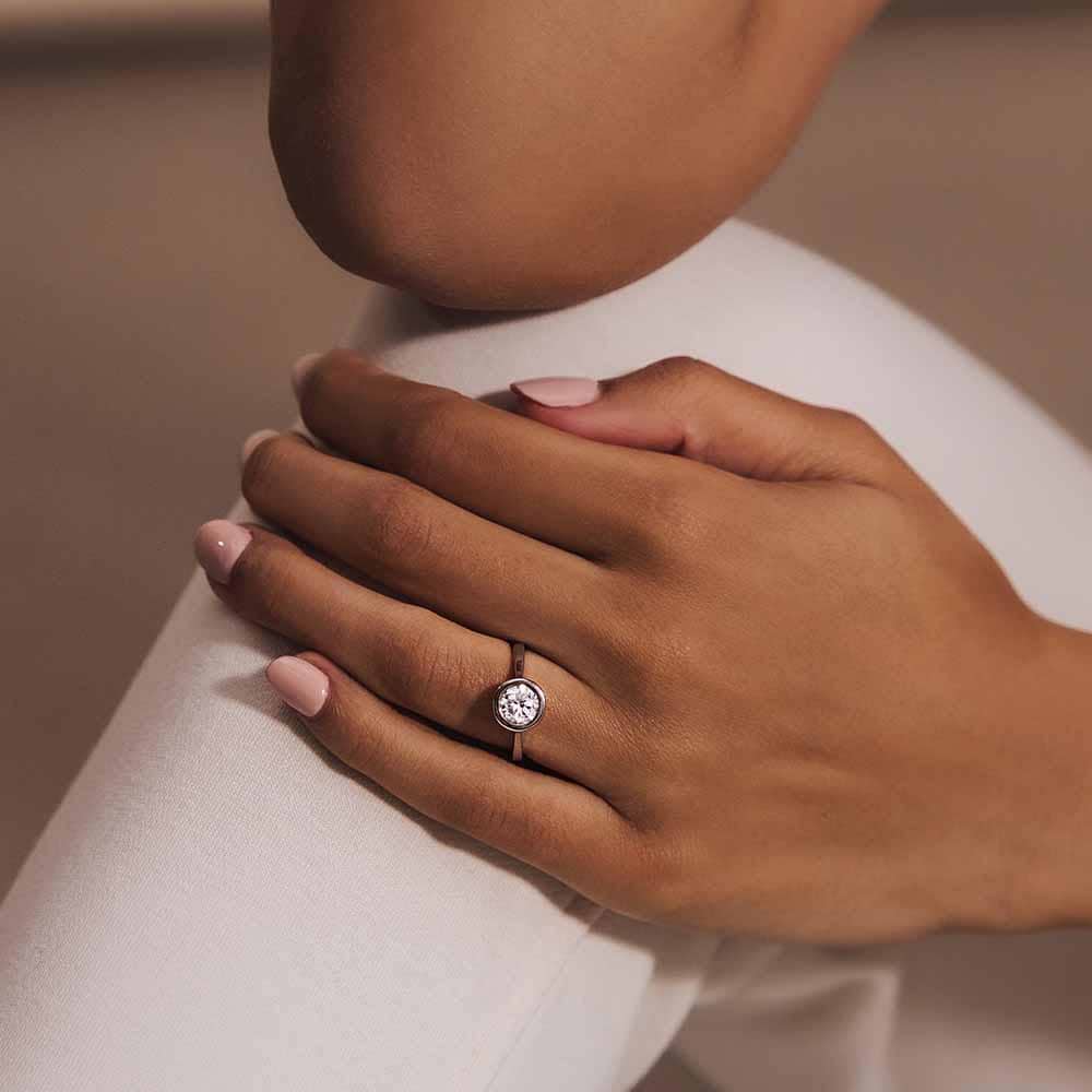 Shown with 1ct Round Cut Lab Grown Diamond in 14k Rose Gold|Elegant modern engagement ring with 1ct round cut bezel set lab grown diamond in 14k rose gold worn on hand