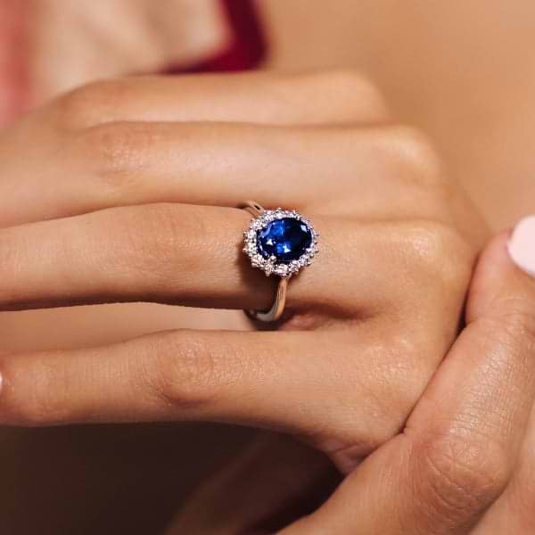 Shown with 3ct Oval Cut Lab Grown Blue Sapphire in 14k White Gold|Gorgeous vintage style engagement ring with floral design halo around a 3ct lab grown blue sapphire in 14k white gold worn on hand