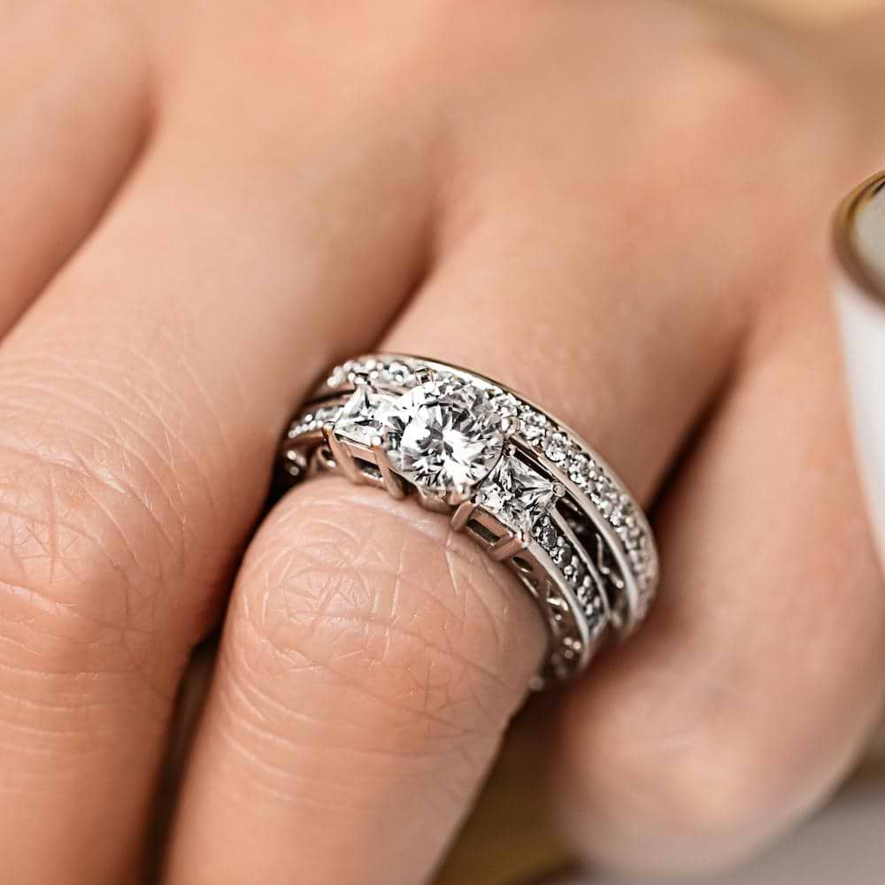 Shown with a Round cut center stone and two Princess cut Lab-Grown Diamonds side stones with scroll detailing and accenting diamonds on the band in recycled 14K white gold 