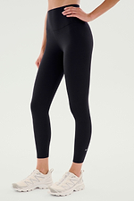 A person wears SPLITS59 Airweight High Waist Legging in black with white athletic sneakers, standing against a plain light background—ideal for hot yoga.