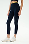 A person stands against a plain background wearing SPLITS59 Dual High Waist Airweight 7/8 leggings in Indigo/Ray with a yellow waistband, white athletic shoes, and a matching navy top—ideal for hot yoga.