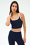 A woman wears the SPLITS59 Cait Rigor Bralette in Indigo/White, styled with matching leggings, standing against a plain light background and touching her neck.